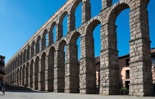 An ancient aqueduct with multiple arches and built of robust stone, under a clear blue sky,