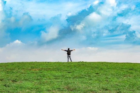 View of a backpacker man spreading his arms on a hill. Successful backpacker on top of a hill