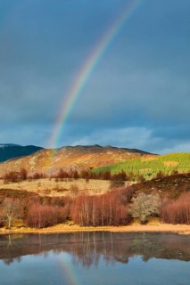 Atmospheric cloudy sky with rainbow over mountainous, partly wooded Highlands in the west of
