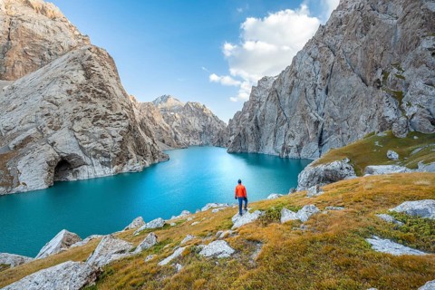 Young man at the turquoise mountain lake Kol Suu with rocky steep mountains, Kol Suu Lake, Sary