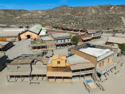 Western town with wooden houses and a dry, mountainous landscape on a sunny day, aerial view, Fort