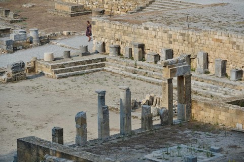 Ruins of an ancient temple with stone columns and a visitor near stone walls, Kamiros,