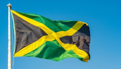 The flag of Jamaica flutters in the wind, isolated against a blue sky