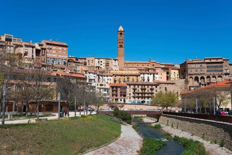 Historic town with a central stone tower, river in the foreground and several residential buildings