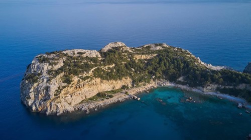 Drone shot, Dense vegetation covers a rocky island surrounded by crystal clear sea, Anthony Quinn