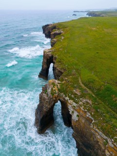Steep coastline with characteristic rock arches and thundering waves crashing against the rocks,