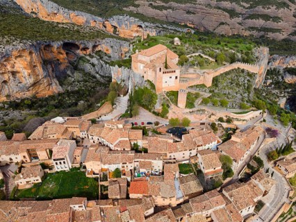 A historic village with tiled roofs and a fortress, nestled in a mountainous landscape, aerial