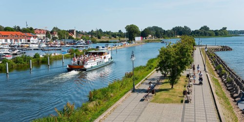 River promenade with people and a ship on the water of a coastal town, Gizycko,