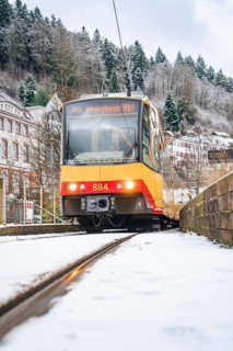 Front view of a tram on snow-covered tracks, surrounded by trees and buildings, Bad Wildbad, Black