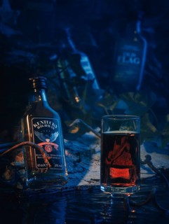 Whisky bottles and a glass of whisky in a blue night scene with water and shadows