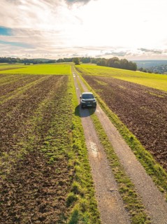 Black car driving on a narrow country lane through wide fields under a cloudy sky, Carsharing, VW