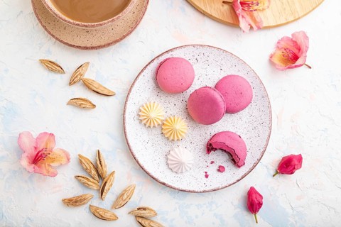 Purple macarons or macaroons cakes with cup of coffee on a white concrete background decorated with