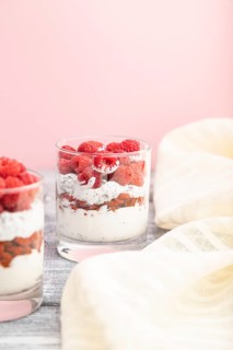 Yogurt with raspberry, goji berries and chia seeds in glass on gray and pink background and linen
