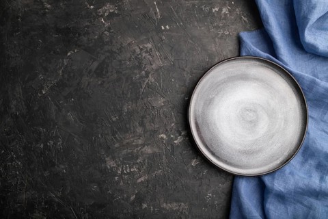 Empty gray ceramic plate on black concrete background and blue linen textile. Top view, copy space,