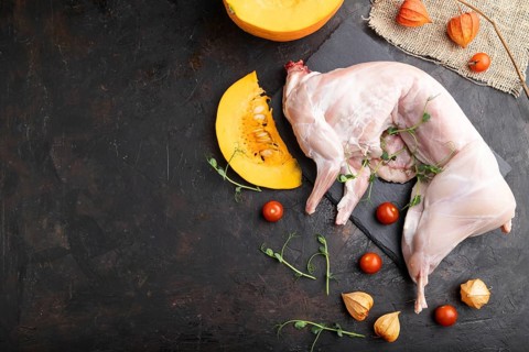Whole raw rabbit with pumpkin, tomatoes, pea sprouts on a black concrete background and linen