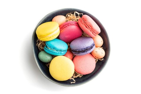 Multicolored macaroons and chocolate eggs in blue ceramic bowl isolated on white background. top