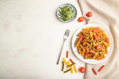 Tortiglioni semolina pasta with tomato and microgreen sprouts on a white wooden background and