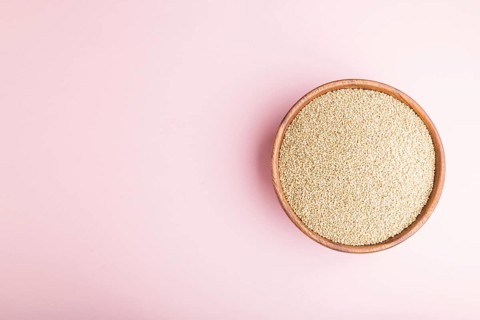 Wooden bowl with raw white quinoa seeds on a pastel pink background. Top view, flat lay, copy space