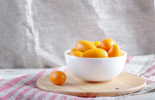 Kumquats in a white plate on a wooden kitchen board, close up