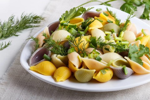 Conchiglie colored pasta with fresh greengrocery on a linen tablecloth on white wooden background.