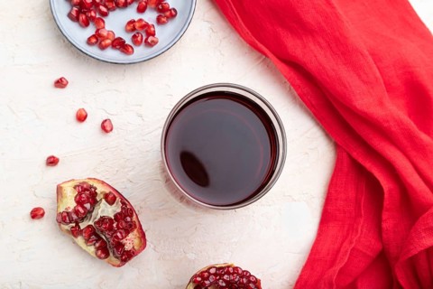Glass of pomegranate juice on a white concrete background with red textile. Top view, close up,