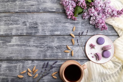 Purple macarons or macaroons cakes with cup of coffee on a gray wooden background and white linen