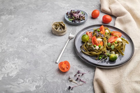 Tagliatelle green spinach pasta with tomato, pea and microgreen sprouts on a gray concrete