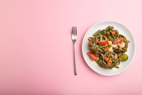 Tagliatelle green spinach pasta with tomato, pea and microgreen sprouts on a pastel pink background