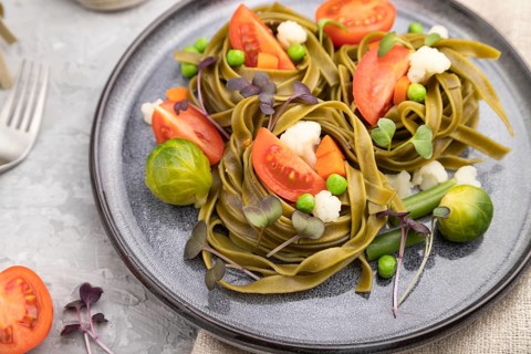 Tagliatelle green spinach pasta with tomato, pea and microgreen sprouts on a gray concrete