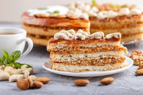 Piece of homemade cake with caramel cream and nuts with cup of coffee on a gray concrete background