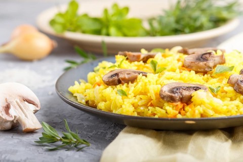 Yellow fried rice with champignons mushrooms, turmeric and oregano on blue ceramic plate on a gray