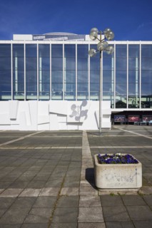 Front of the Musiktheater im Revier in front of a blue sky with lanterns and flower pots in