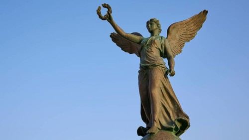 Angel statue with raised hand and outstretched wings towards the sky, harbour area, Rhodes Town,
