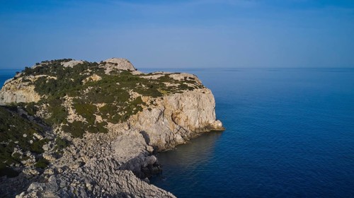 Drone shot, A rocky coastline with steep cliffs, calm sea and a clear blue sky, Anthony Quinn Bay,