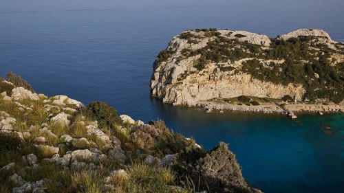 Rocky coastal landscape with green vegetation and calm blue water, Anthony Quinn Bay, Vagies Bay,