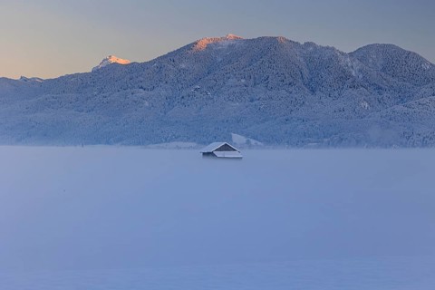 Hut in the snow in front of mountains, evening light, view of Rabenkopf and Benediktenwand,