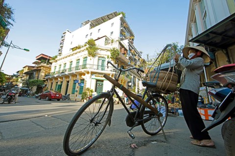 Vietnamese woman with conical hat prepares her bicycle for her sales tour through the Old Quarter,