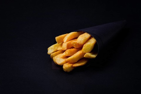 French fries, in black paper packaging, on a black background, close-up, selective focus