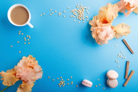 Orange iris flowers and a cup of coffee on a blue pastel background. Morninig, spring, fashion