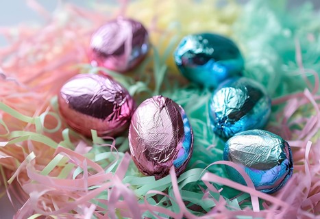 Small chocolate Easter eggs wrapped in shiny foil, placed on a bed of shredded pastel-colored