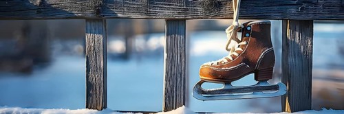 Pair of vintage ice skates hanging by their laces on an old wooden fence with frost and snow gently