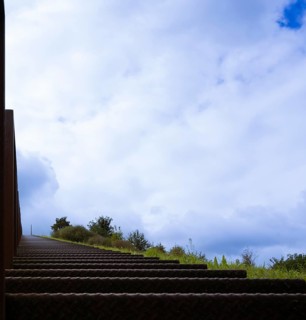 Steep metal stairs, brown, railing at the edge of the picture, green meadow and green bushes on the