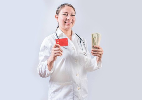 Beautiful and smiling female doctor holding money and credit cards. Happy female doctor holding