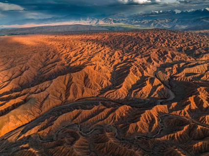 River bed runs through a landscape of eroded hills, badlands at sunset, mountain peaks of the Tian