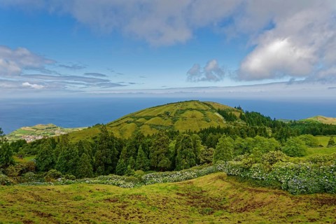 Distant view over green volcanic cones to the sea and clear sky, Caldeira das Sete Cidades, Sete