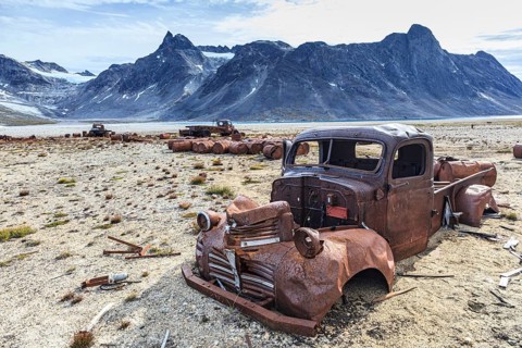Rusty cars and oil drums in front of steep mountains, remains of a US airbase from the Second World