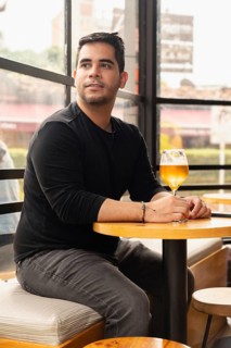 Handsome young Latino man sitting in a cafe with a glass of beer, gazing out the window. The cozy