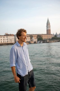 Young man in striped shirt and shorts on the banks of the Grand Canal, behind Campanile, Venice,