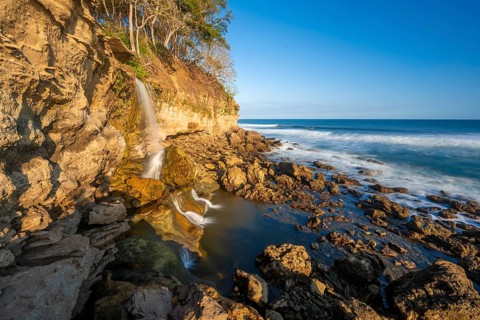 Waterfall falls into the sea on the cliffs, Catarata el Chorro, coastal landscape in the evening