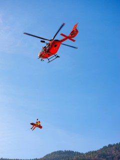 Injured person in a mountain bag with an air rescuer being winched into the rescue helicopter